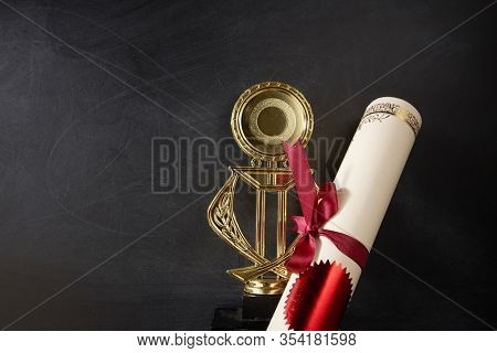 Golden trophy and certificate over blackboard background. top view. flat lay.Trophy is a specific achievement, serves as recognition / evidence of merit, awarded for sporting events