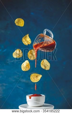 Sauce In Glass Jar And Tasty Potato Chips Falling Into Blow With Tomato Ketchup Frozen In The Air. P