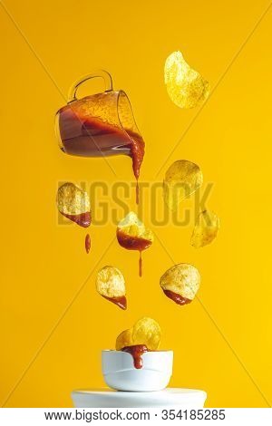 Sauce In Glass Jar And Tasty Potato Chips Falling Into Blow With Tomato Ketchup Frozen In The Air. P