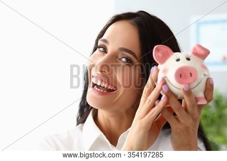 Beautiful Woman Shows Piggy Bank And Smiles. Selection Suitable Items In Stores From Customers Price