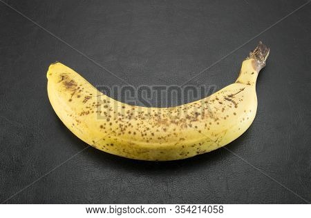 Yellow Overripe Banana With Brown Dots On A Black Leather Background. Tropical Stale Fruit