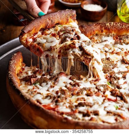 Deep Dish Meat Pizza On A Wooden Table With A Slice Being Pulled
