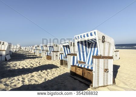 Wicker Chairs On Beach, Aligned, On Sylt Island, At North Sea, Germany. Beach Scenery On A Hot Day O