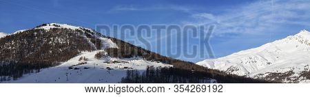 Panorama Of Snowy Ski Slope With Ski-lifts, Traces And Forest In High Winter Mountains And Cloudy Su