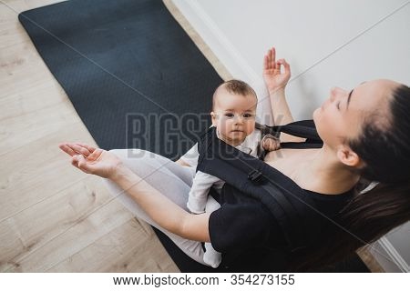 Young Mother Doing Yoga Exercises And Meditation With Her Little Baby In Ergo Backpack.