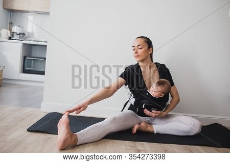 Young Mother Doing Yoga Exercises And Meditation With Her Little Baby In Ergo Backpack.