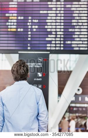Rear view of mature man looking at his flght on screen in airport