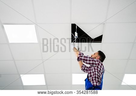 Full Length Portrait Of Electrician On Stepladder Installs Lighting To The Ceiling In Office
