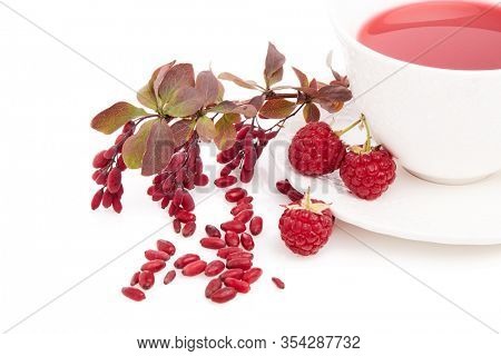 Healthy fruit tea with barberries and raspberries in white cup and branch of berberry isolated on white background.