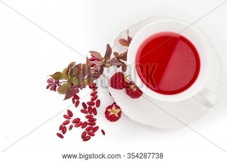 Healthy fruit tea with barberries and raspberries in white cup and branch of berberry isolated on white background. Top view