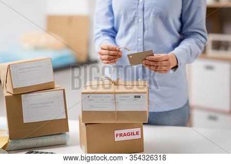 delivery, mail service, people and shipment concept - close up of woman packing parcel box and tying tag by rope at post office