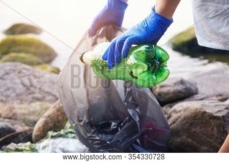 Volunteer Young Woman Collecting Garbage, Holding Full Bag Of Waste And Plastic Bag, Land And Water 