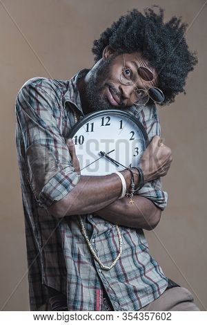 A Curly-haired Dominican With Open Glasses On His Glasses Embraces A Large Wall Clock And Smiles