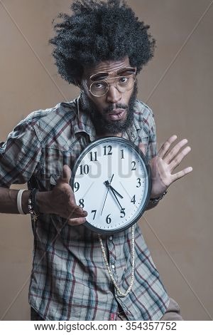 A Curly-haired Dominican With Open Glasses On His Glasses Embraces A Large Wall Clock And Smiles