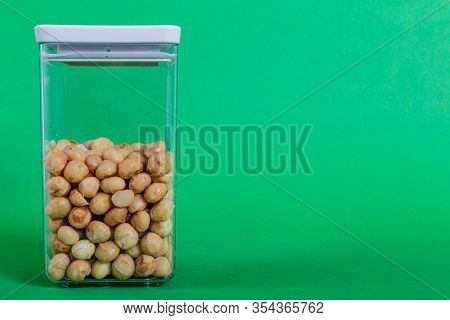 Macadamias Inside A Transparent Plastic Container With A Green Background, Also Called Queensland, B