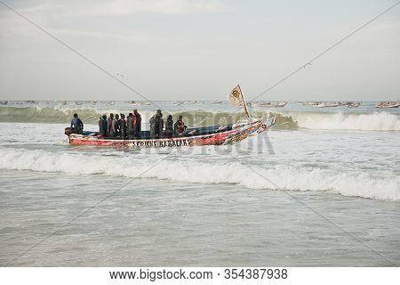 Kayar, Senegal - January 17, 2020: Fishermans Pushing Traditional Painted Wooden Fishing Boat In Kay