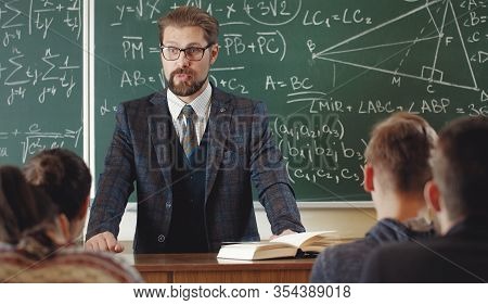 Mathematician In Formal Wear Standing In Front Of Teenage Students In Teaching Room During Lesson