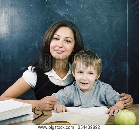 Little Cute Boy In Glasses With Young Real Teacher, Classroom Studying At Blackboard School Kido