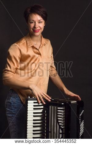 A Brunette In A Gold Shirt, With Short Haircut, On A Dark Kground Of The Studio. With Accordion Musi