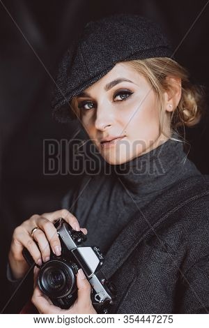 Beautiful Girl Blonde Photographer In A Strict Suit And A Cappie Is Holding An Old Retro Camera In H