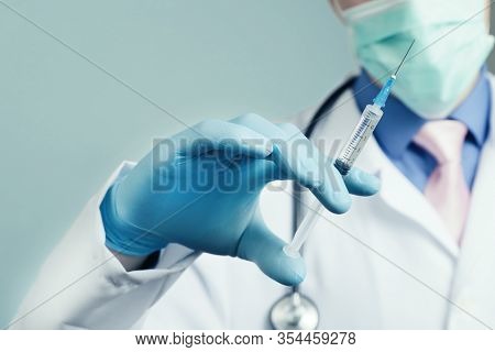 Doctor In Gauze Mask And Medical Robe Holding Syringe In His Blue Rubber Glove Dressed Hand. Health 