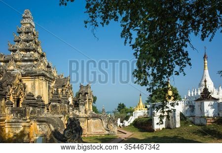 Burmese heritage architecture. Yellow moldy walls of Maha Aungmye Bonzan Monastery and white and golden pagodas in Inwa (Ava), Myanmar