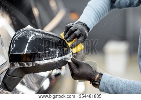 Man Applying Sticking Protective Film On A Car Mirror At The Vehicle Service Station, Cllose-up. Con