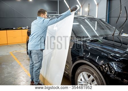 Man Preparing Protective Film For Sticking On A Car Body, Taking It From The Roll At The Vehicle Ser