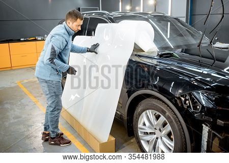 Man Preparing Protective Film For Sticking On A Car Body, Marking It To With A Pen At The Vehicle Se