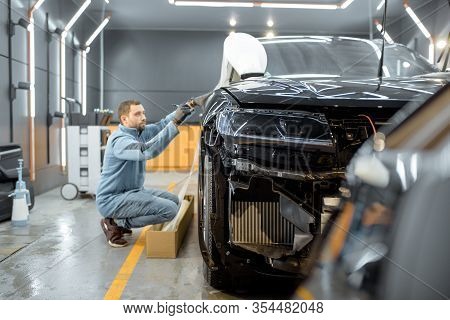 Man Preparing Protective Film For Sticking On A Car Body, Marking It To With A Pen At The Vehicle Se
