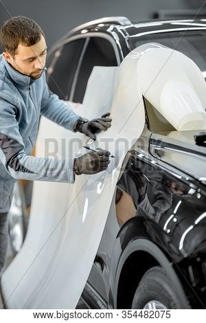 Man Preparing Protective Film For Sticking On A Car Body, Marking It To With A Pen At The Vehicle Se
