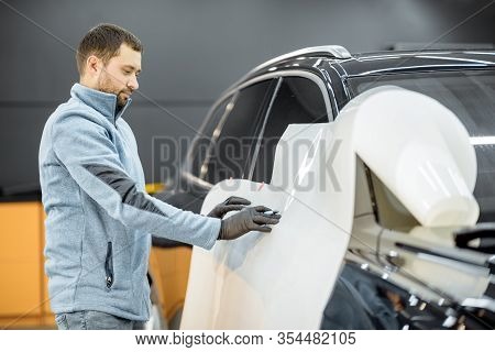 Man Preparing Protective Film For Sticking On A Car Body, Marking It To With A Pen At The Vehicle Se