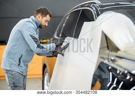 Man Preparing Protective Film For Sticking On A Car Body, Marking It To With A Pen At The Vehicle Se
