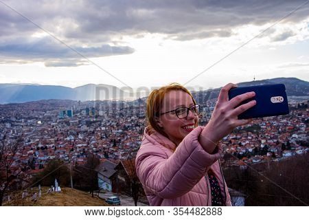 Girl With Glasess And Brown Hair Taking Selfie Above Sarajevo With Mobile Phone