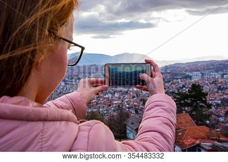 Girl With Glasess And Brown Hair Photographing Sarajevo With Mobile Phone