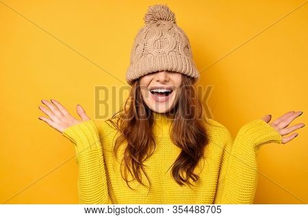 A Girl In A Yellow Sweater Stands On A Yellow Background With A Cap Pulled Over Face And Laughs, Spr