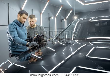 Two Car Service Workers Inspecting Vehicle, Measuring Paint Cover Thickness Of The Car Body At The V