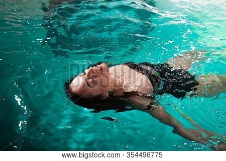Beautiful Girl Is Relaxing In The Spa Pool,swim And Relax. Young Woman Floating In Water On The Back