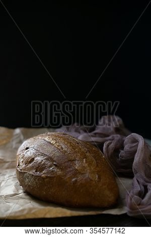 Whole Loaf Of Rye Or Wheat Dark Bread On Parchment Paper On Black Background. Hot Fresh Wholegrain P