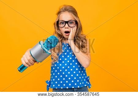 Portrait Of Young Caucaian Girl With Long Fair Hair In Black Glasses With A Microphone Interwiews An