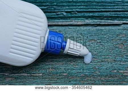 White Plastic Tube With A Drop Of Glue On A Green Wooden Board