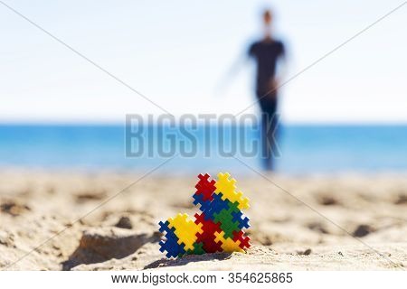Autism Awareness Day Concept. Colorful Puzzle Autism Awareness Heart On Beach Sand And Silhouette Of
