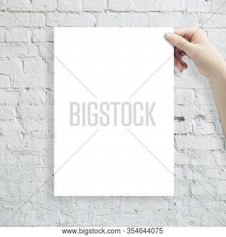 Hand Holding White Blank Poster On Brick Wall Background. Presentation Concept.