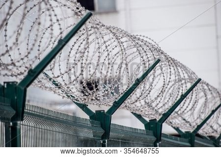 Swirls Of Barbed Wire Over The Fence. The Fence Symbolizes Prison, Non-freedom, Totalitarianism And 
