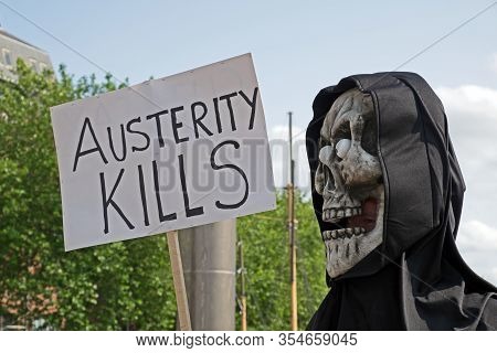 Bristol, Uk - July 8, 2015: A Masked Anti-austerity Demonstrator Holds A Placard With The Slogan 