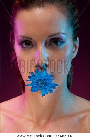 Suggestivo ritratto di una bella donna con un fiore blu nella sua bocca, studio su nero