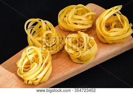 Pasta Alluovo, Tagliatelle Pasta, Round Balls Of Raw Pasta On The Wooden Cutting Board On Black Back
