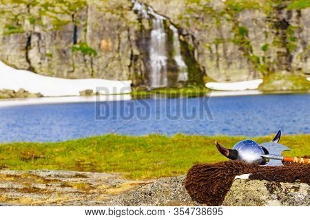 Viking Helmet With Axe On Lake Shore In Norway. Tourism And Traveling Concept
