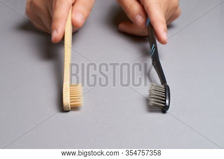 Two Hands Holding Different Types Of Toothbrushes. Plactic And Eco Bamboo Brush. Black And Light Col