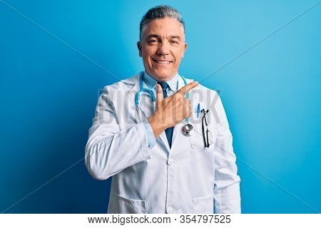 Middle age handsome grey-haired doctor man wearing coat and blue stethoscope cheerful with a smile on face pointing with hand and finger up to the side with happy and natural expression